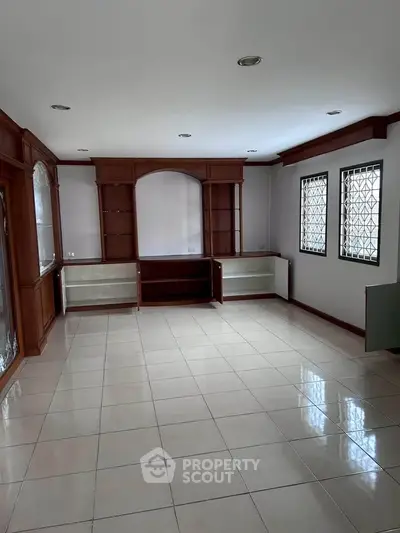 Spacious living room with built-in wooden shelves and tiled flooring