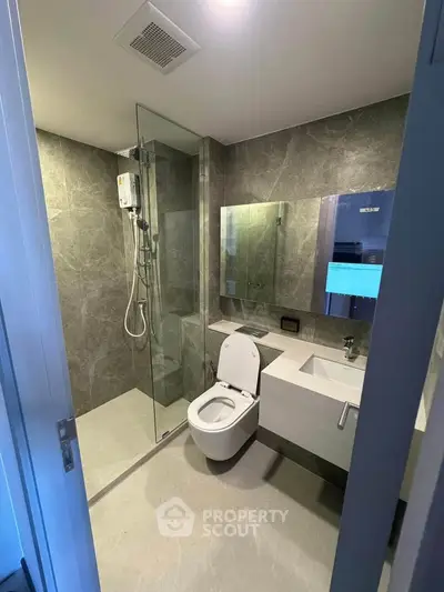 Modern bathroom with sleek design, featuring a glass shower enclosure and wall-mounted toilet.