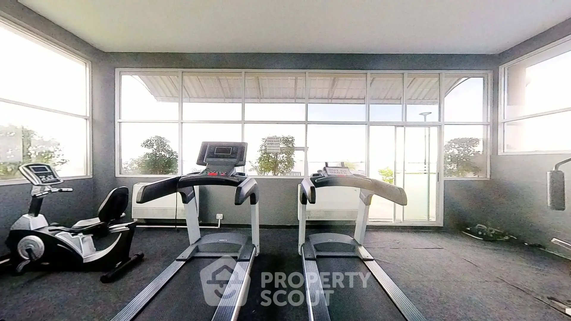 Spacious gym with modern equipment and large windows offering natural light.