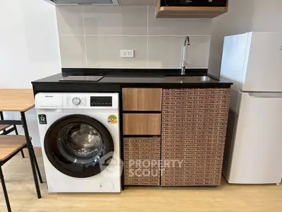 Modern kitchen with washing machine, fridge, and sleek cabinetry in compact layout.
