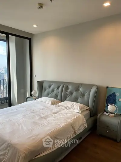 Modern bedroom with stylish bed and city view from balcony.