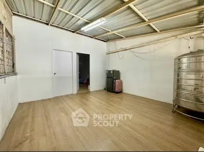 Spacious storage room with wooden flooring and metal tank, ideal for versatile use.