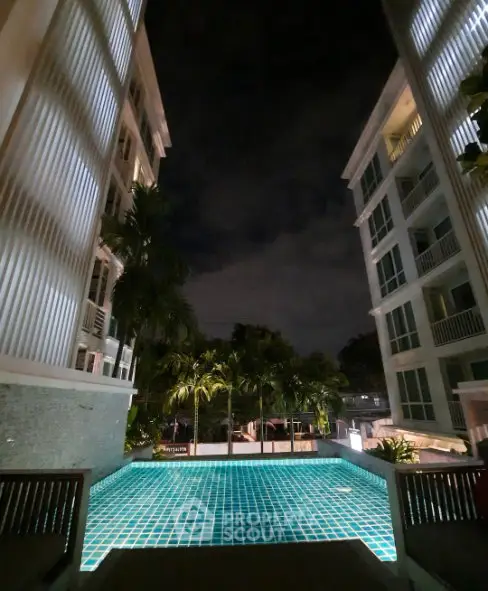 Luxurious night view of a modern apartment complex with illuminated pool and palm trees.