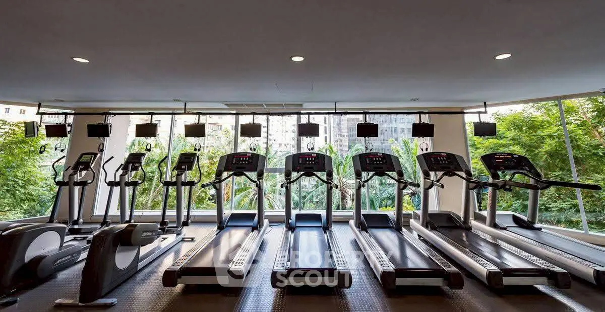 Modern gym with multiple treadmills and large windows offering lush green views.
