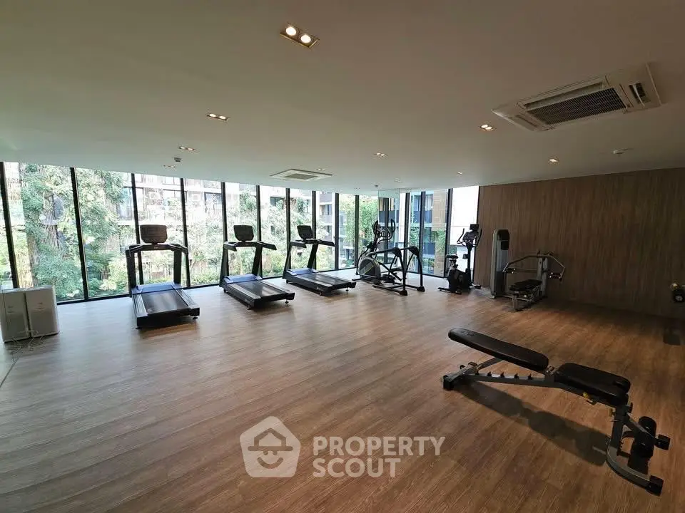 Spacious modern gym with large windows and fitness equipment in luxury building.