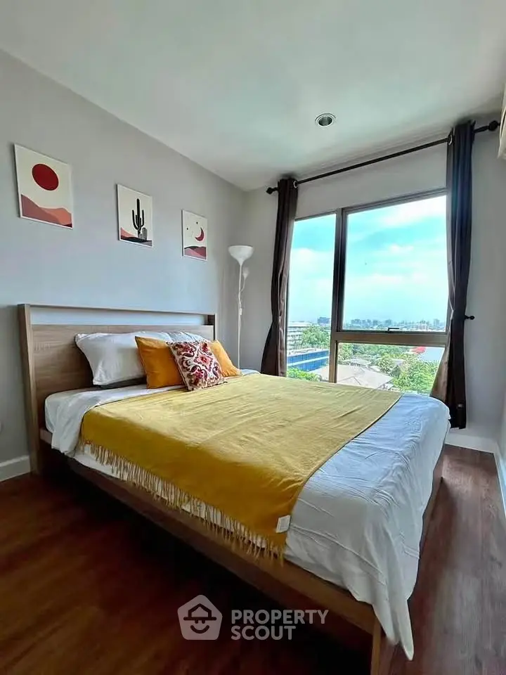Bright and cozy bedroom with large window offering stunning city views, modern decor, and wooden flooring.