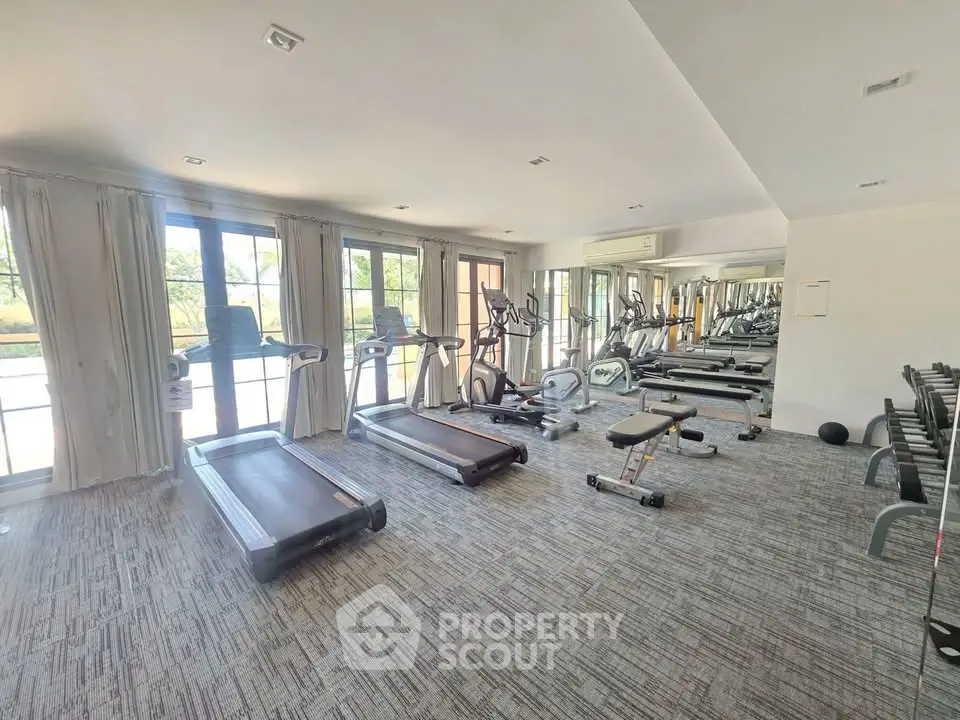 Spacious gym with modern equipment and large windows offering natural light.