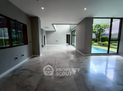 Spacious modern living area with large windows overlooking a pool and garden, featuring sleek marble flooring.