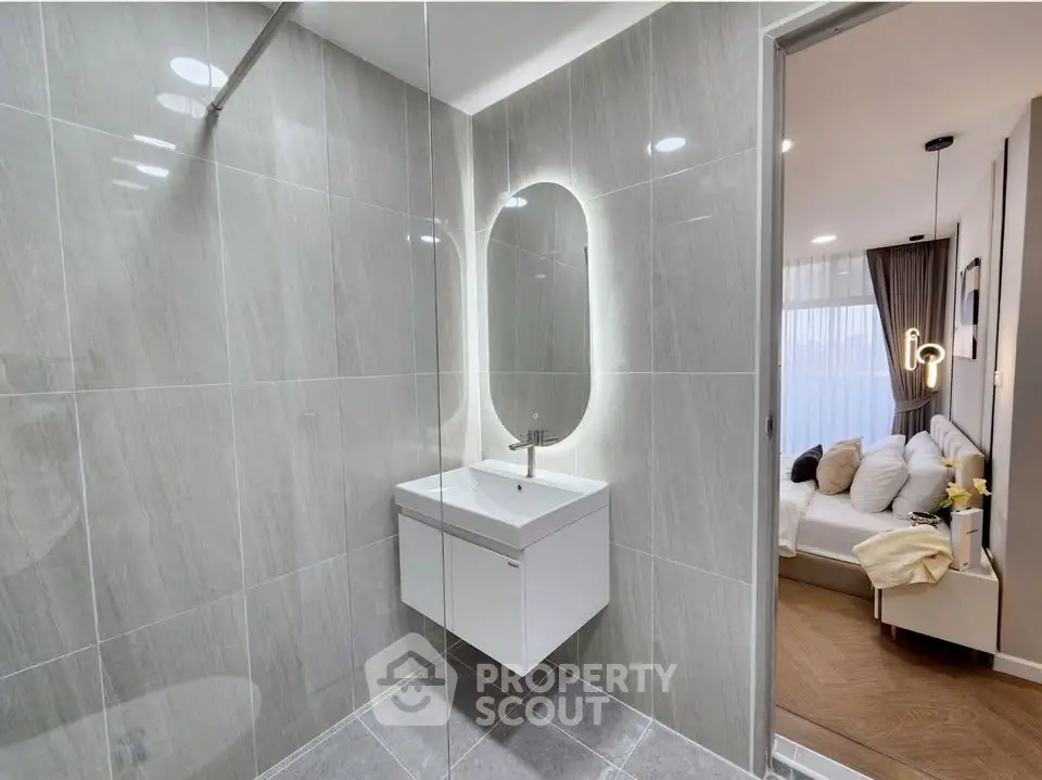Modern bathroom with sleek design and illuminated mirror, adjacent to a cozy bedroom.