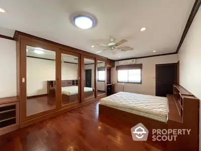 Spacious bedroom with polished hardwood floors, mirrored closet doors, and a ceiling fan, offering a blend of comfort and style.