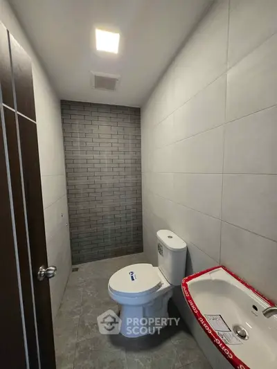 Modern bathroom with sleek design featuring a toilet and compact sink in a tiled space.