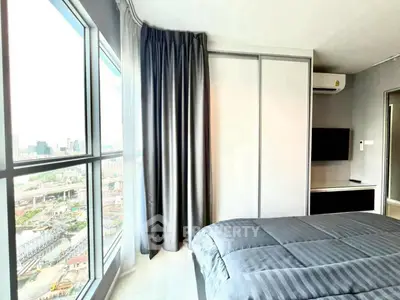Modern bedroom with large window offering stunning city view, sleek furnishings, and cozy ambiance.