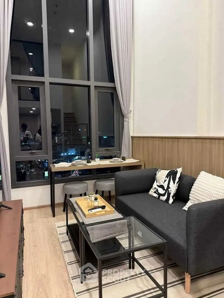 Modern living room with high ceilings and city view, featuring stylish furniture and large windows.