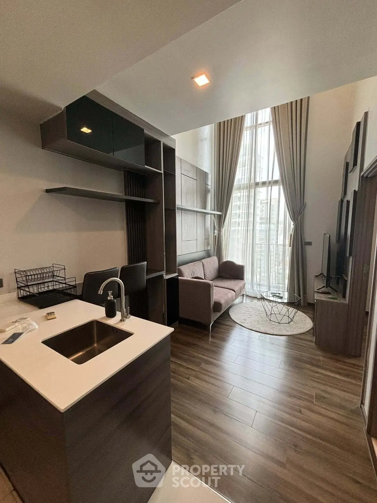 Modern open-layout living room with high ceilings and stylish kitchen area, featuring floor-to-ceiling windows.