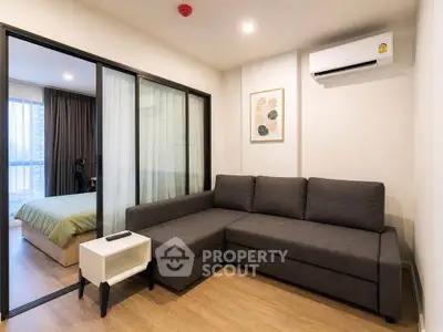 Modern living room with sleek gray sofa and sliding glass doors leading to a cozy bedroom.