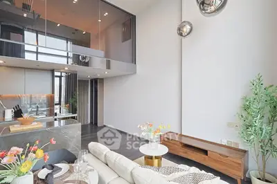 Modern living room with high ceiling and open kitchen layout, featuring stylish decor and ample natural light.