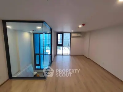 Spacious modern living room with large windows and wooden flooring, featuring a unique glass-enclosed area.