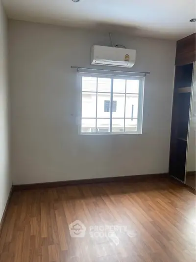 Spacious bedroom with wooden flooring and natural light from window