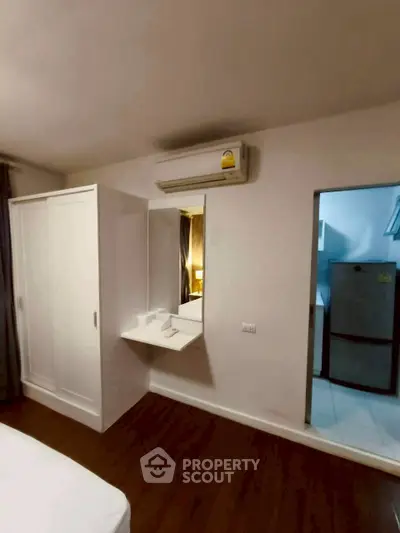 Modern bedroom with built-in wardrobe and air conditioning, adjacent to a compact kitchen area.