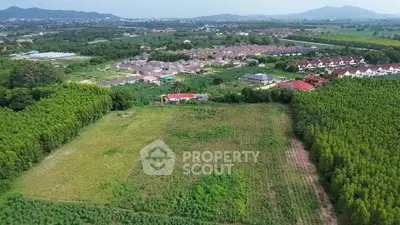 Expansive aerial view of lush green land with nearby residential area and scenic mountains.