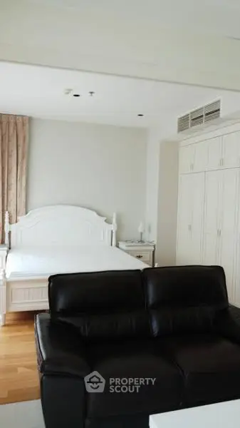 Spacious bedroom with elegant white bed and black leather sofa, featuring ample closet space.