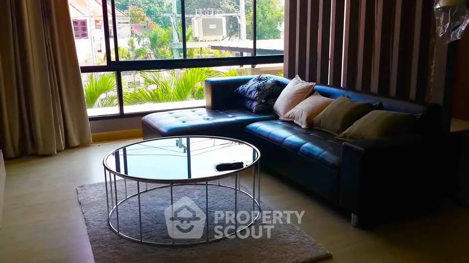 Stylish living room with modern sofa and glass coffee table, featuring large window with garden view.