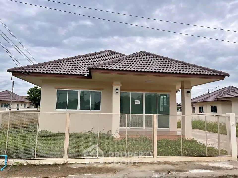 Charming single-story house with tiled roof and fenced yard under cloudy sky.