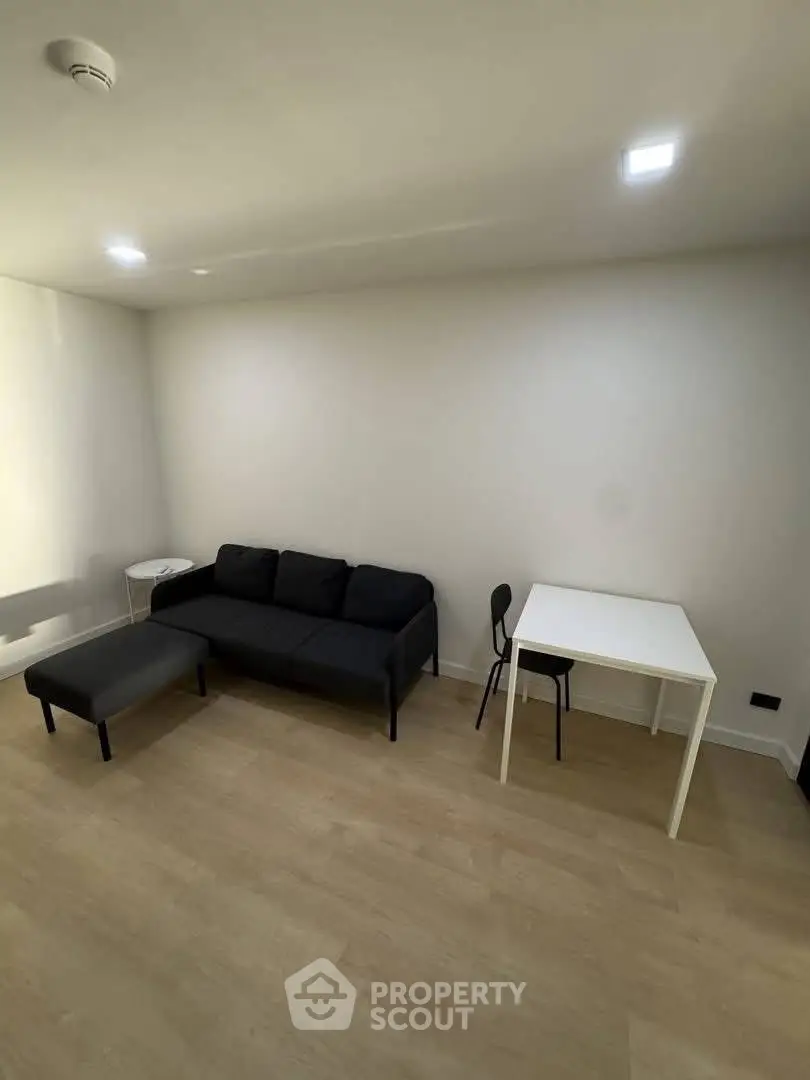 Minimalist living room with black sofa, white table, and wooden flooring.