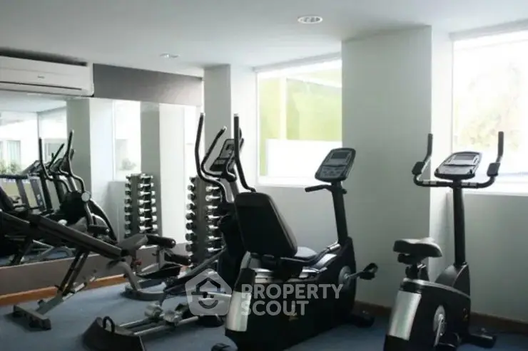 Modern gym with exercise equipment and large windows in a residential building.