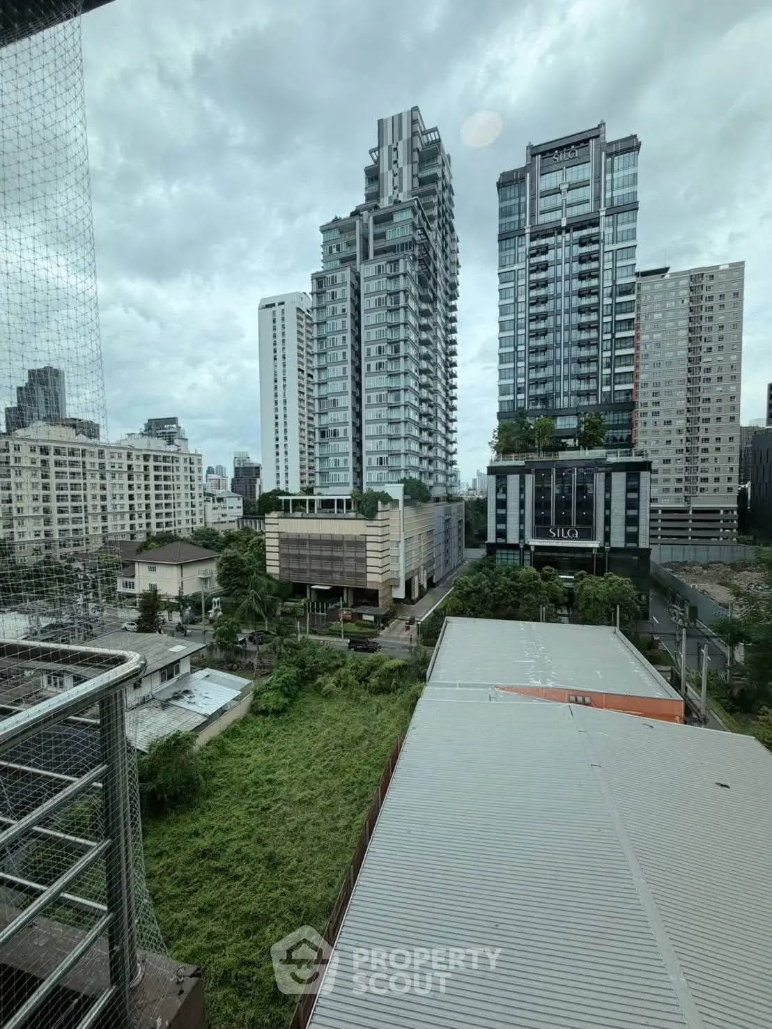Stunning cityscape view from a high-rise balcony overlooking modern skyscrapers and lush greenery.