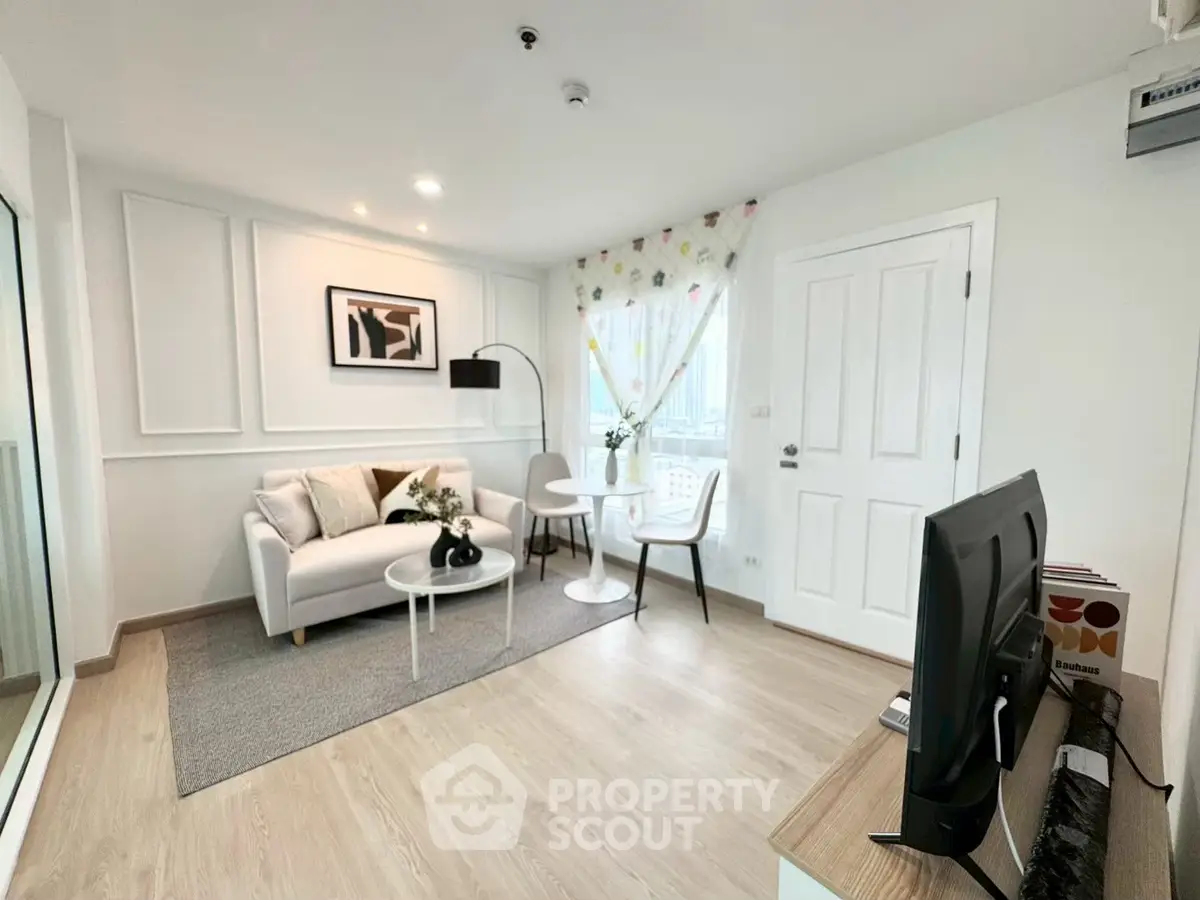 Modern living room with stylish decor and natural light, featuring a cozy seating area and sleek TV setup.