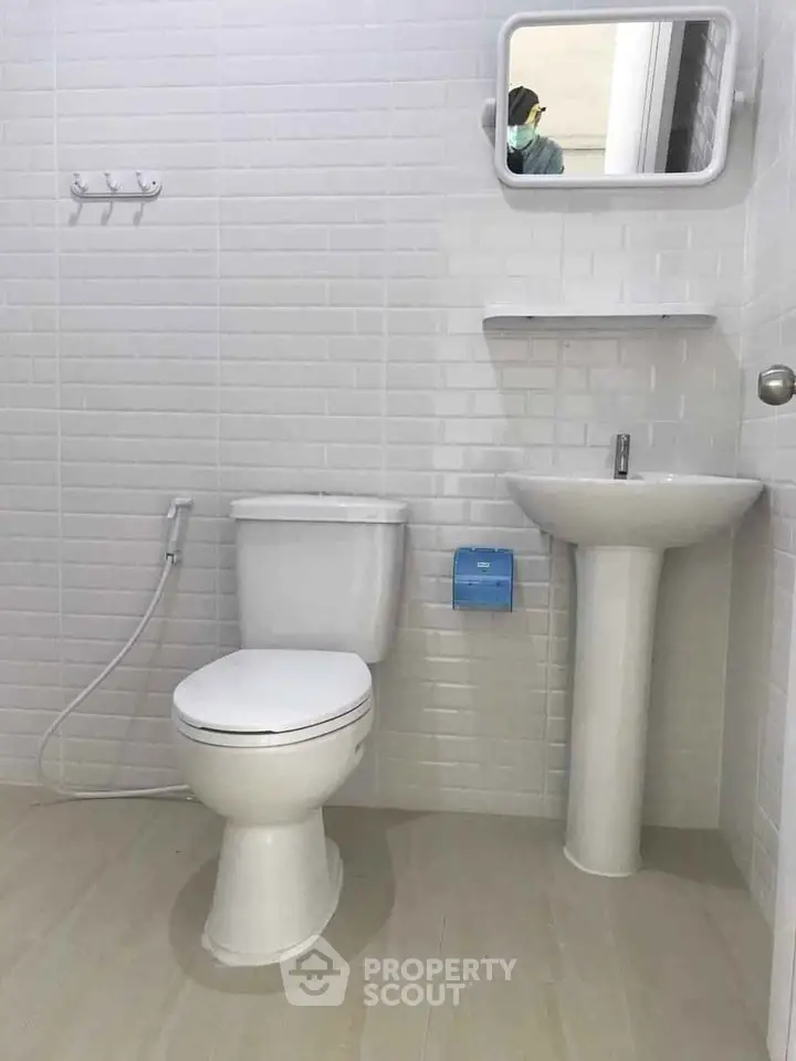 Modern bathroom with white tiles and pedestal sink, featuring a wall-mounted mirror.