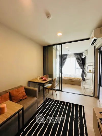 Modern apartment interior with cozy living room and stylish bedroom separated by glass doors.