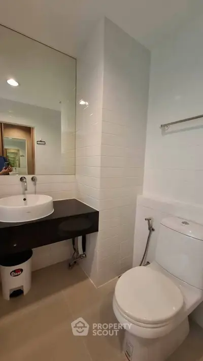 Modern bathroom with sleek fixtures and white tiles, featuring a round sink and toilet.