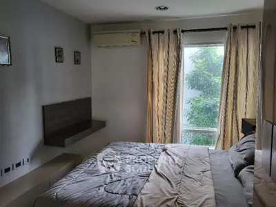 Cozy bedroom with large window and air conditioning, offering a serene view of greenery.