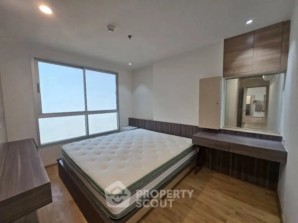Spacious bedroom with large window and modern furnishings in a stylish apartment.