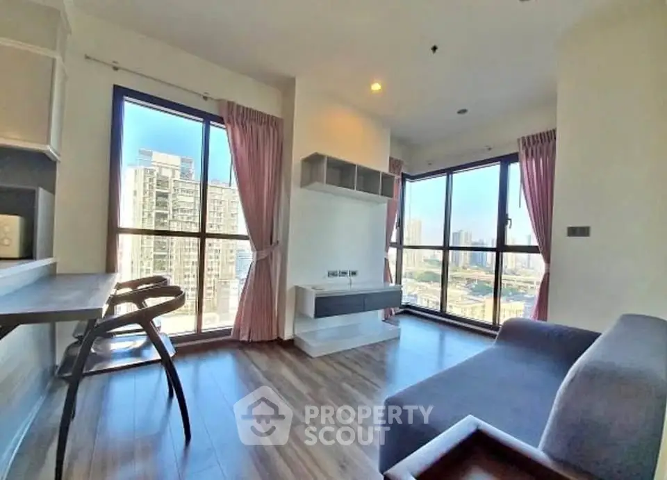 Modern living room with large windows and city view, featuring stylish furniture and wooden flooring.
