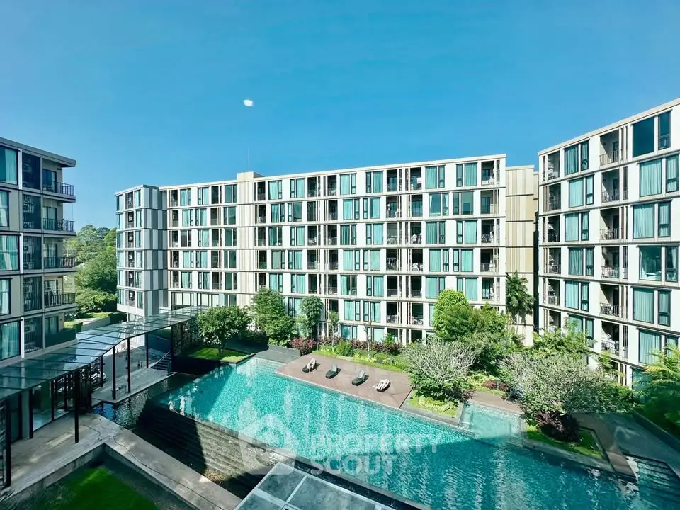 Modern apartment complex with pool and lush greenery under clear blue sky.