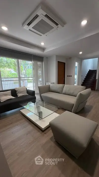 Modern living room with sleek furniture and large windows offering natural light and garden view.