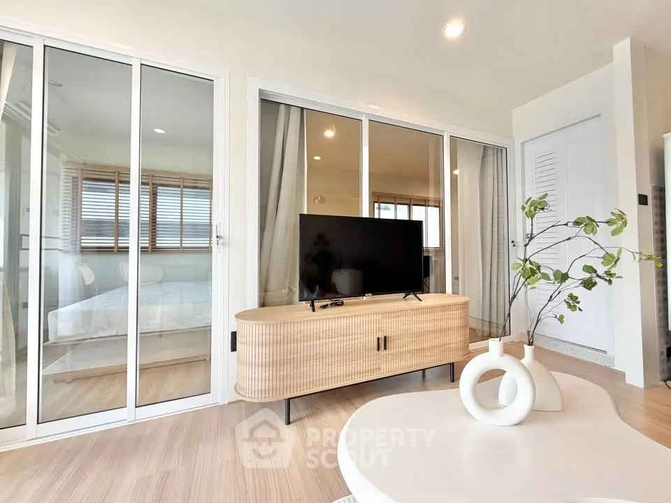 Modern living room with stylish TV stand and glass sliding doors leading to a cozy bedroom.