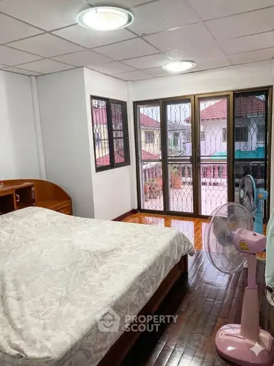 Cozy bedroom with large windows and balcony view, featuring wooden flooring and modern furnishings.