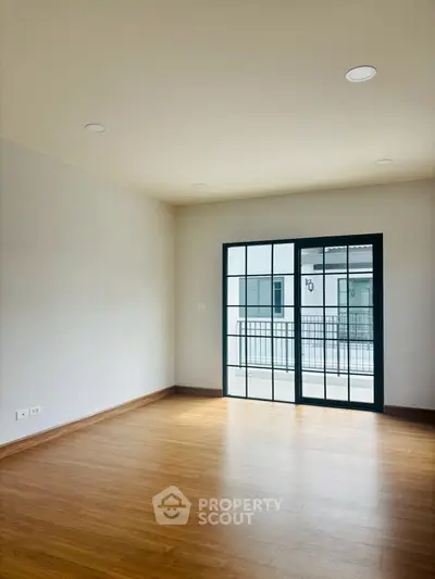 Spacious empty room with wooden flooring and large window for natural light