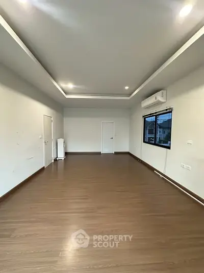 Spacious empty room with wooden flooring and modern ceiling lights, ideal for customization.