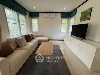 Spacious living room with modern decor, featuring a large sofa, flat-screen TV, and natural light.