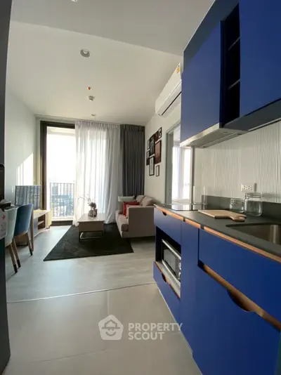 Modern open-plan living room with stylish blue kitchen cabinets and balcony view.