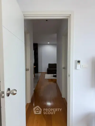 Modern apartment hallway with wooden flooring leading to a cozy living area.