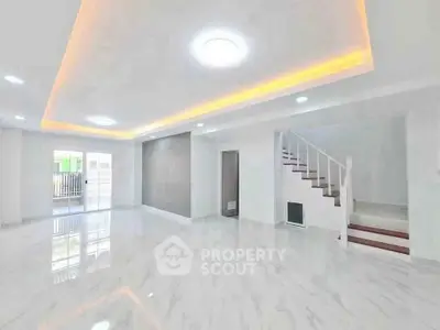 Spacious modern living room with elegant lighting and staircase in a bright open layout.