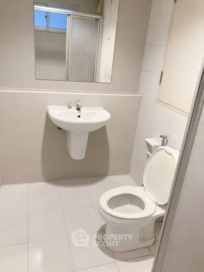 Modern bathroom with white fixtures and tiled walls, featuring a sleek sink and toilet.