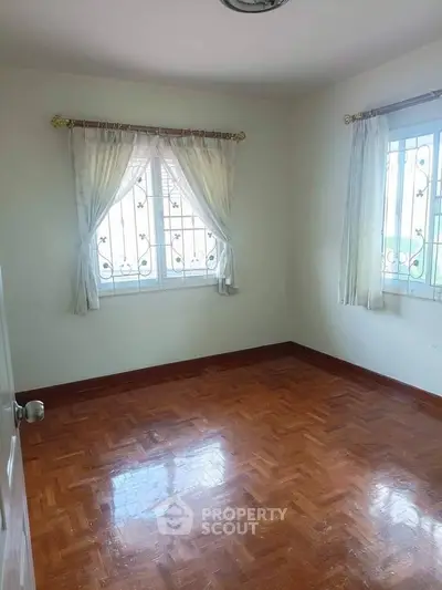 Spacious empty room with wooden flooring and large windows for natural light.