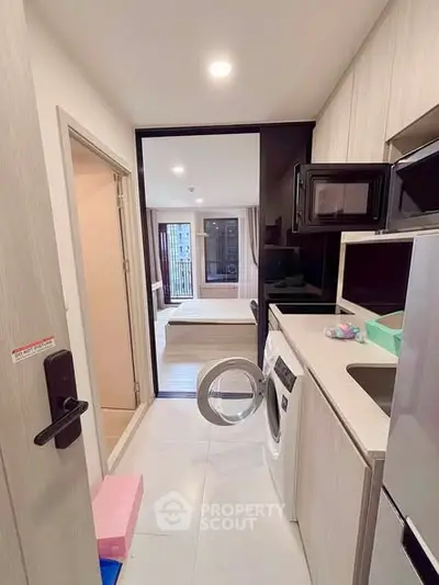 Modern compact kitchen with washing machine and microwave, leading to a cozy living area with balcony view.